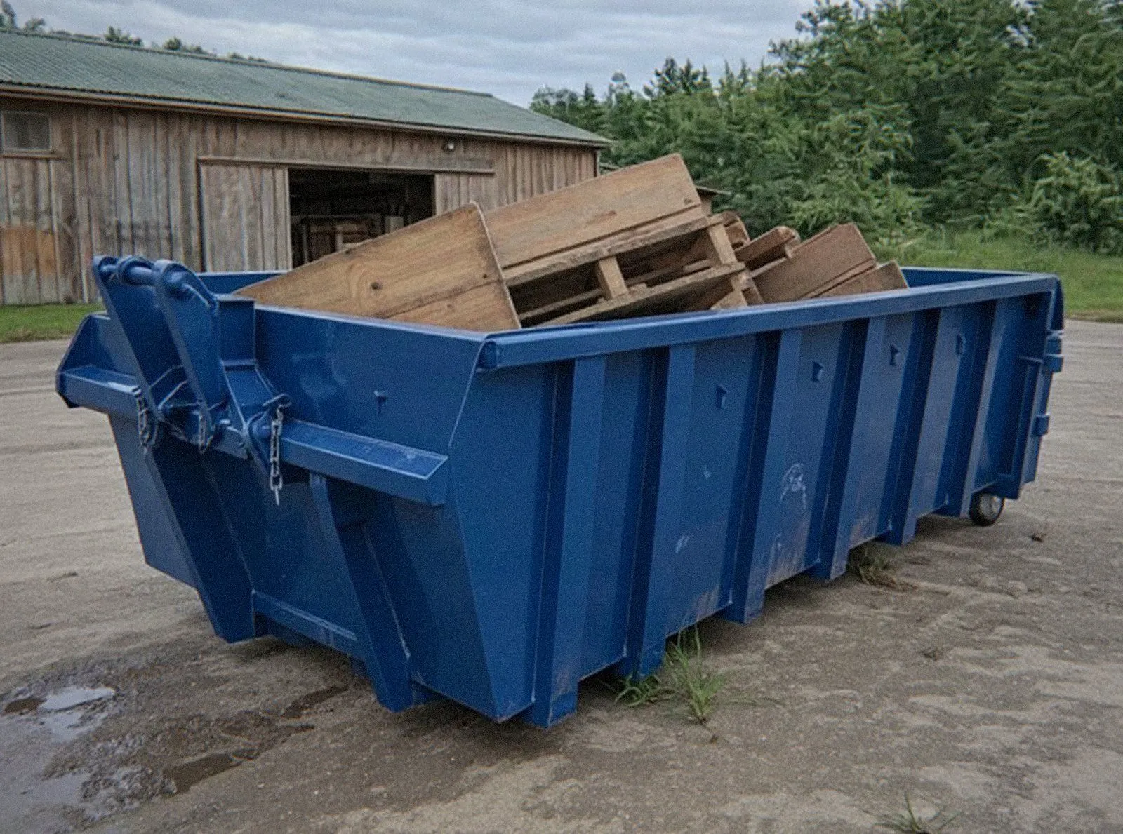 Benne bleue remplie de palettes et de vieilles planches derrière un atelier de Haguenau, location de benne pour déchets de bois