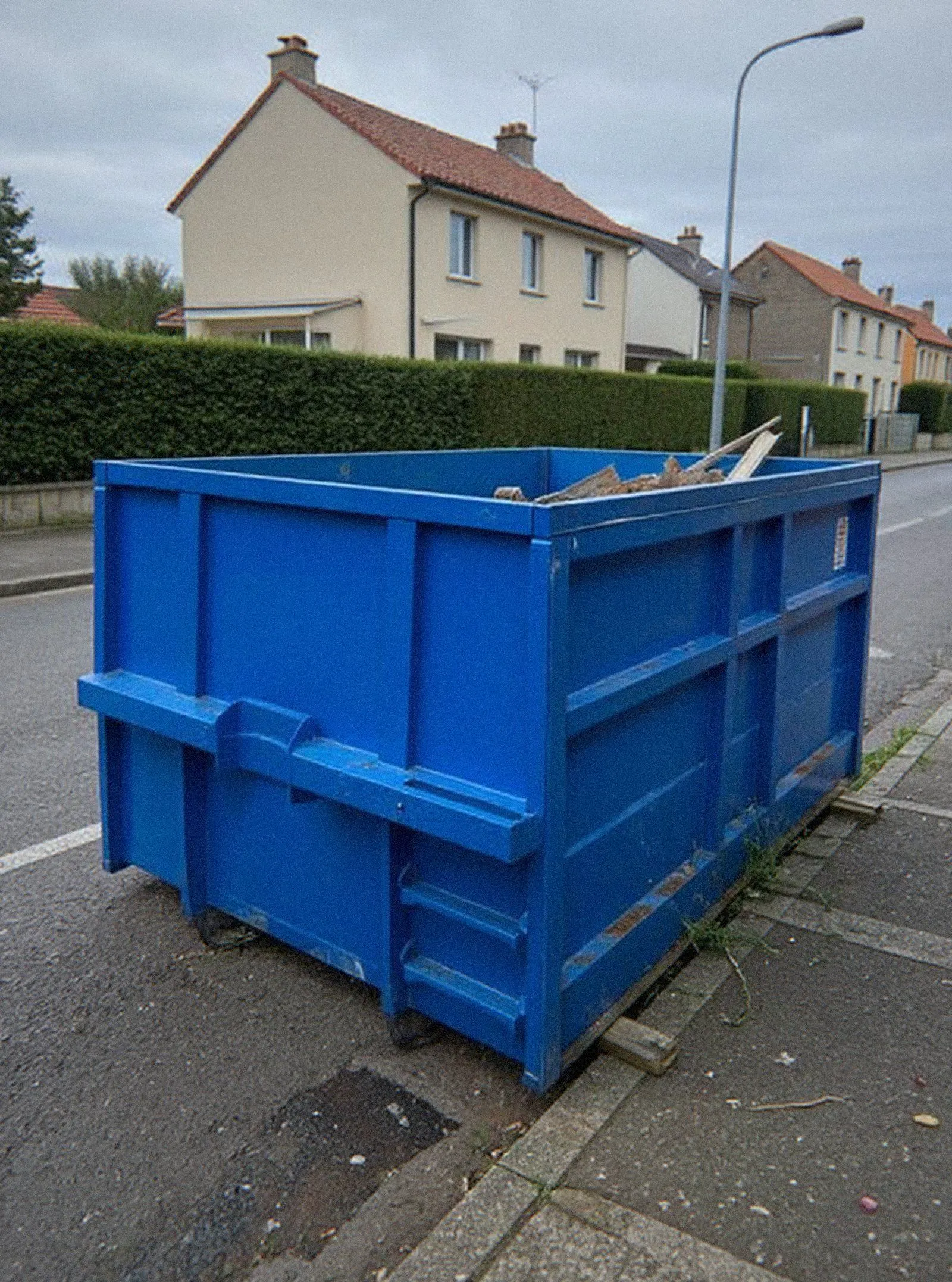 Benne bleue livrée sur des madriers le long d'un trottoir à Haguenau